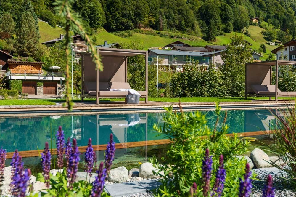 Hotelzwembad met ligbedden en Alpenpanorama in een groene omgeving
