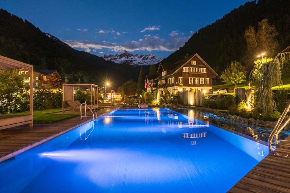 Verlicht hotelzwembad bij nacht voor een bergdorp en de Alpen
