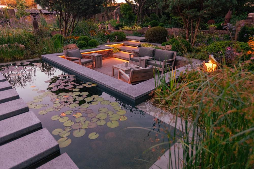 Lounge aan natuurlijk zwembad met waterlelies en avondlicht