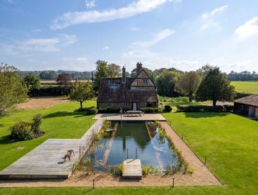 Rechthoekige natuurlijke vijver van Biotop achter een oude boerderij