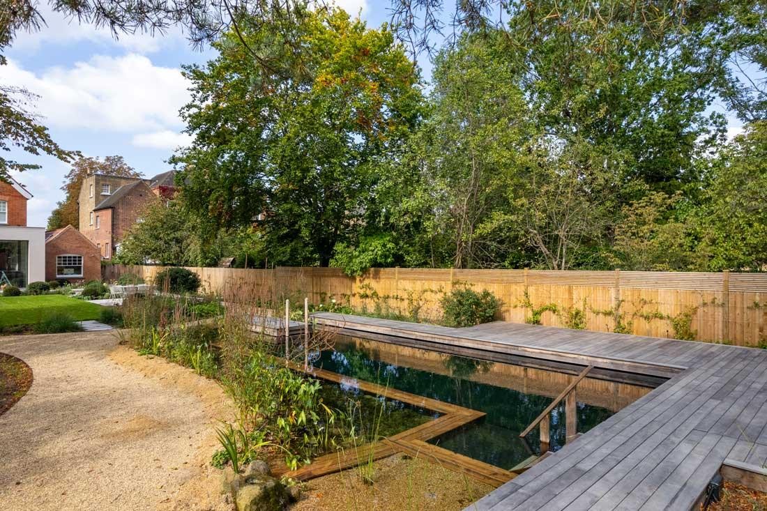Natuurzwembad met houten vlonder voor modern tuinhuis in groene tuin