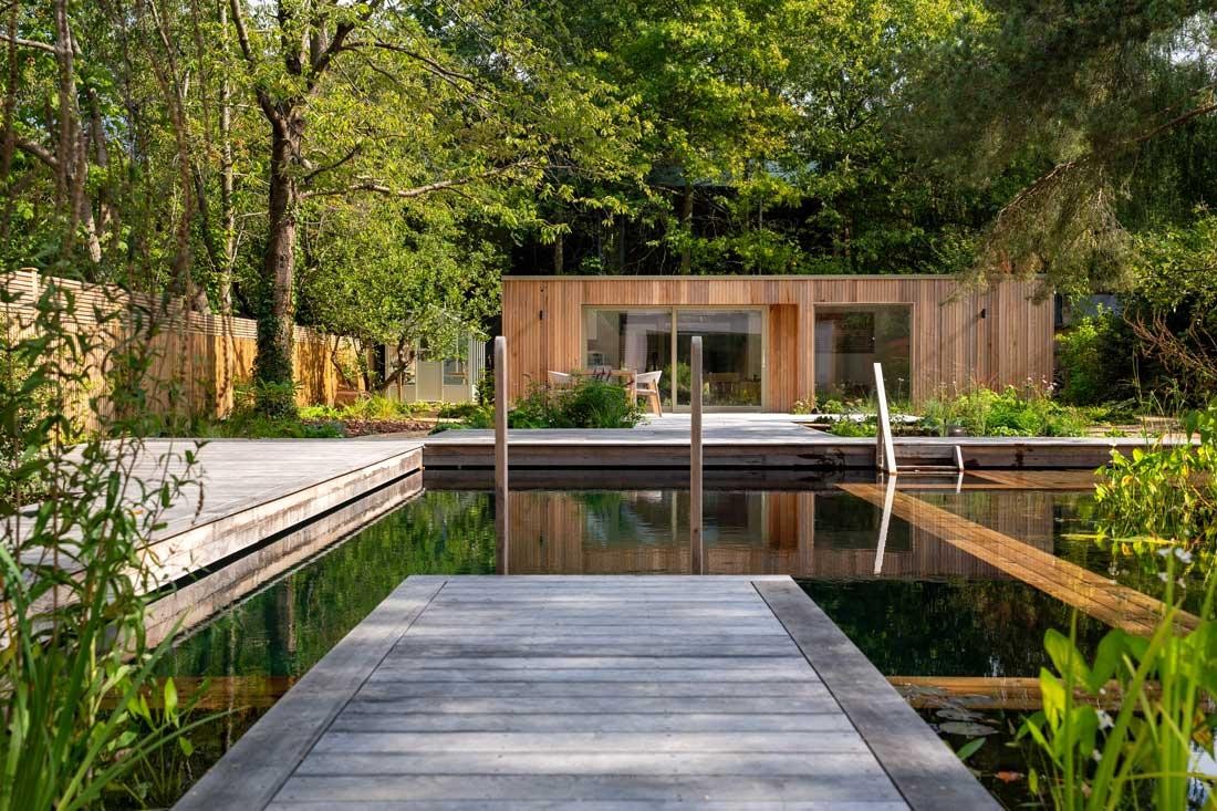 Natuurzwembad met regeneratiezone en houten vlonder in natuurlijke tuin