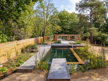 Natuurzwembad met houten terras in grote stadstuin voor bakstenen huis
