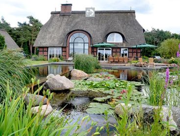 Dromerig tuinlandschap met een traditioneel huis met rieten dak en een zwemvijver