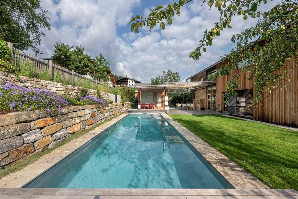 Moderne biopool in de tuin met houten huis en natuurstenen muur
