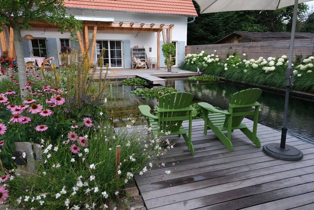 Natuurlijke zwemvijver met houten terras groene stoelen en bloementuin