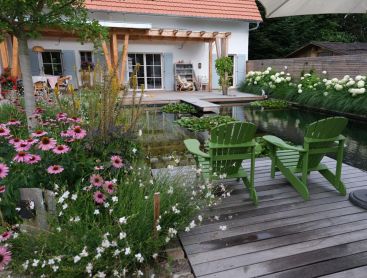 Natuurlijke zwemvijver met houten terras groene stoelen en bloementuin
