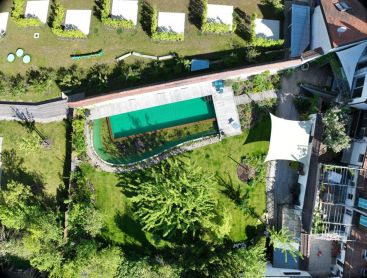 Natuurlijke zwemvijver van boven met houten dek en natuurtuin