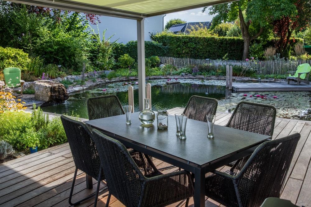Terras met eettafel en uitzicht op zwemvijver in natuurlijke tuin