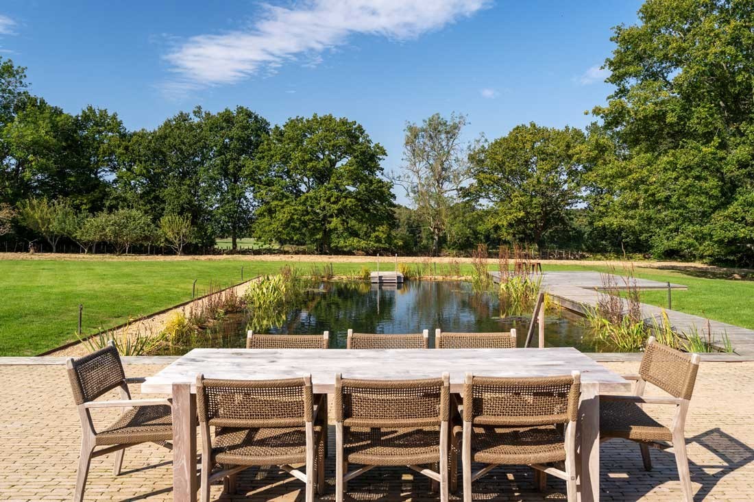 Tuinmeubelen op een terras in eigen tuin naast een zwemvijver