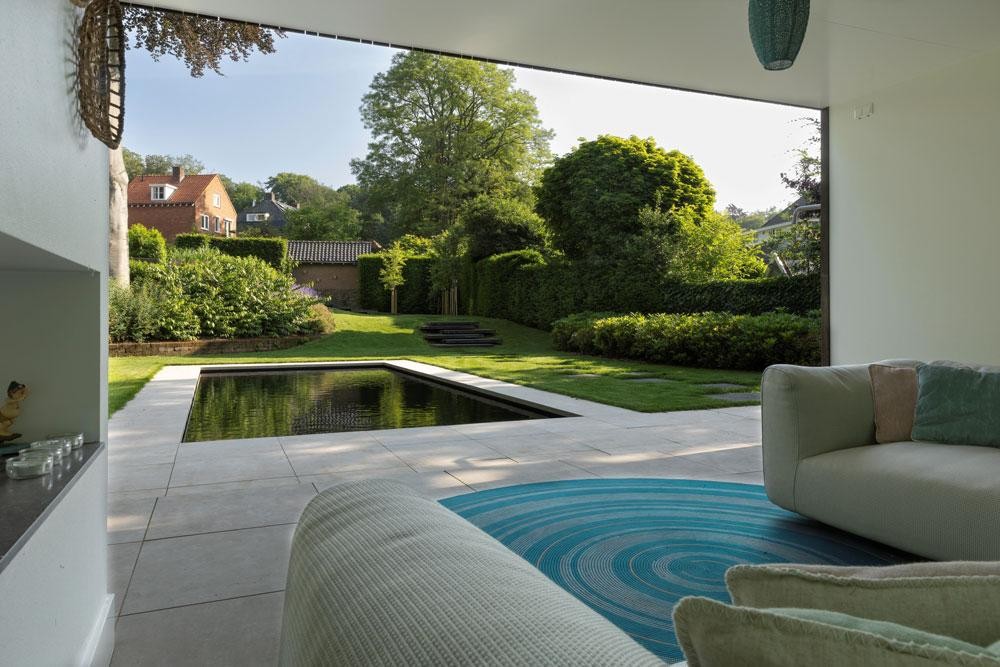 Uitzicht vanuit de lounge op natuurpool, terras en groene tuin