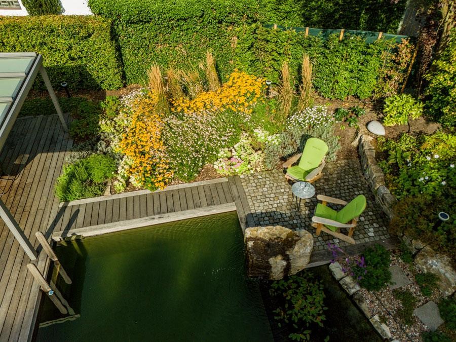 Zitplek aan de zwemvijver met bloembed en groene stoelen