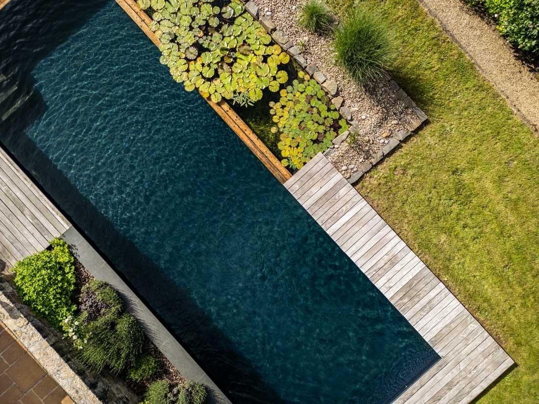 Zwemvijver van boven met waterlelies en houten vlonder