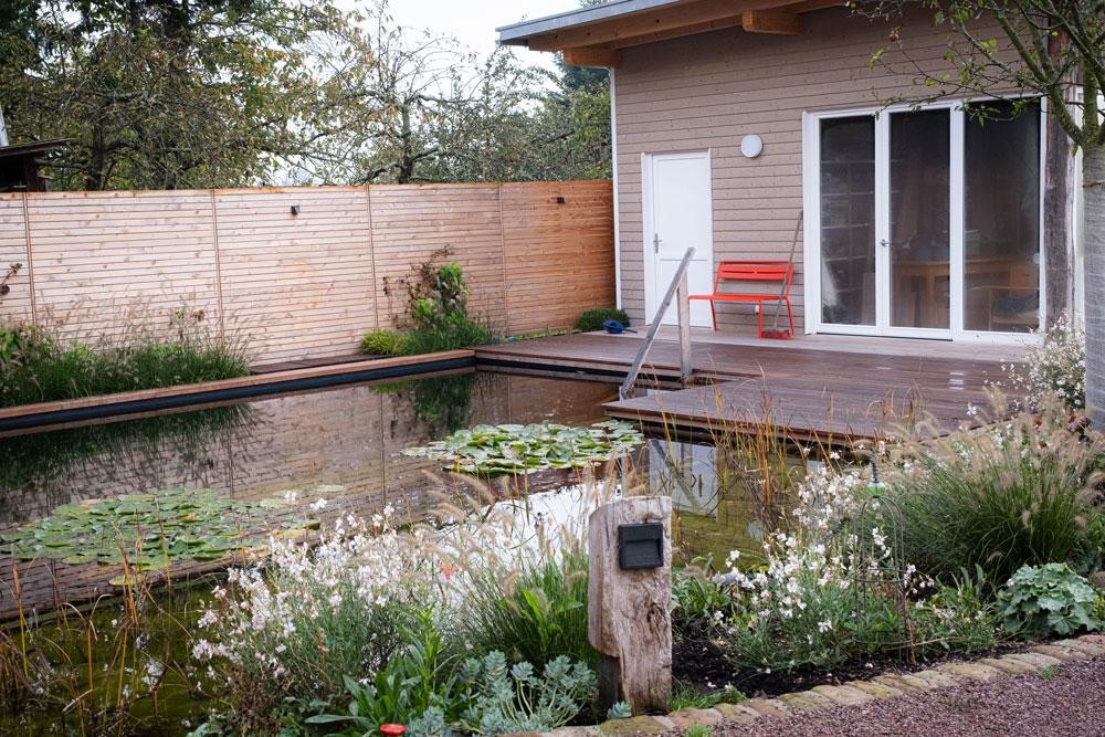 Zwemvijver met houten terras houten huis en natuurlijke tuin